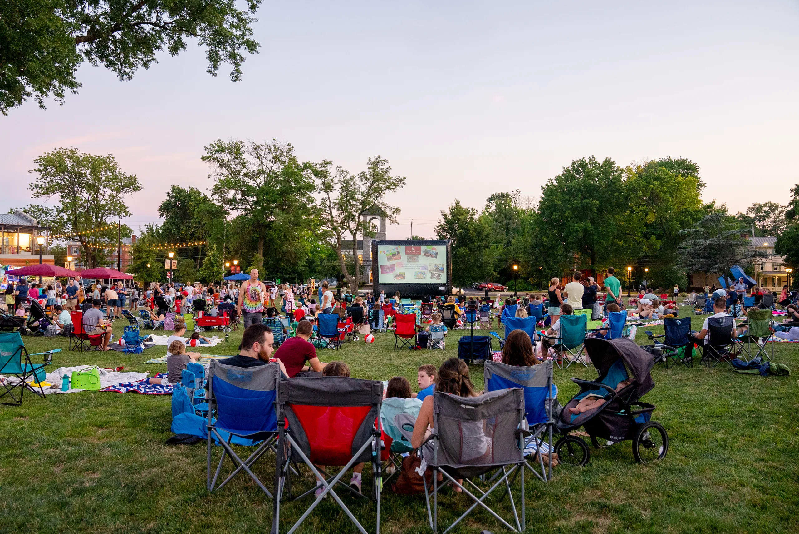 An audience on Berman Lawn facing the outdoor screen at dusk