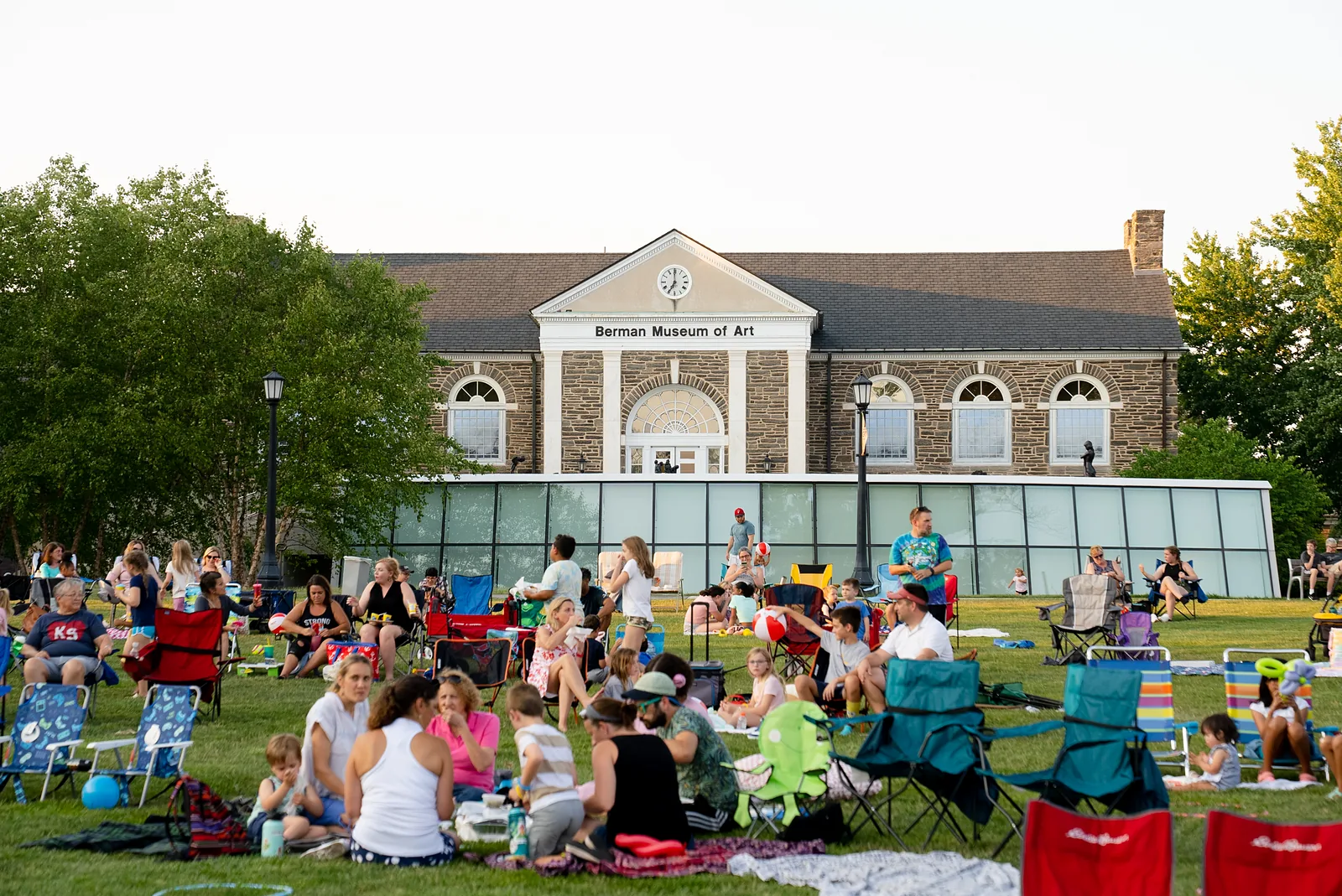 Families on Berman Lawn at dusk for Movies on the Lawn, with an outdoor screen and Bomberger Hall behind