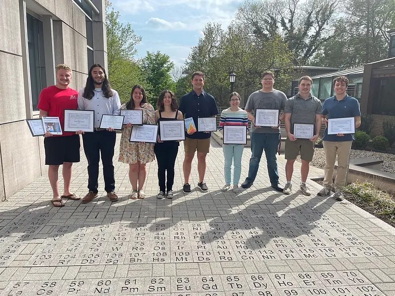 Award recipients standing on the periodic-table paving of the plaza outside the IDC