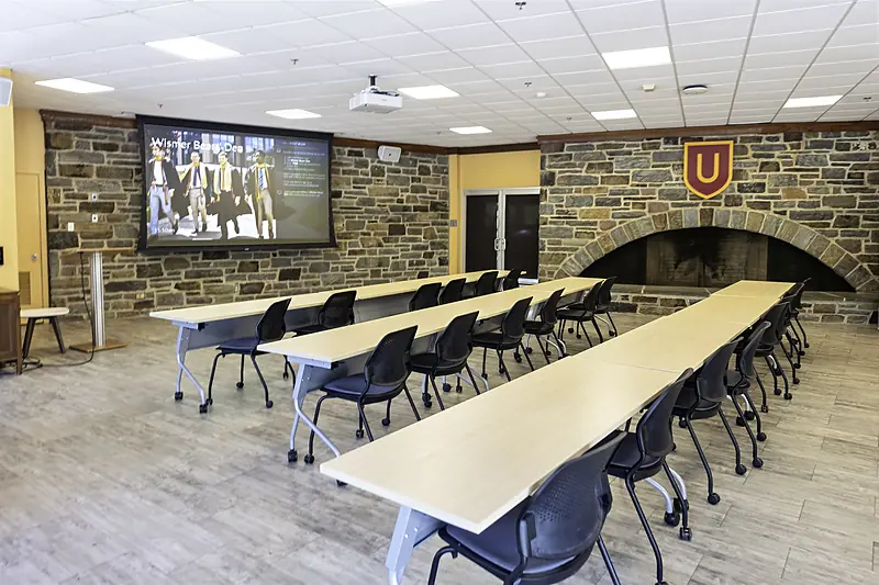 Bears' Den set with rows of tables facing the screen, beside a stone wall and arched fireplace